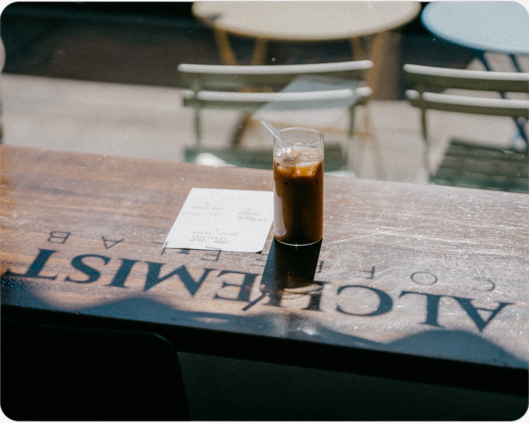 A glass of iced chai and a handwritten menu card on a table branded Alchemist Coffee Lab